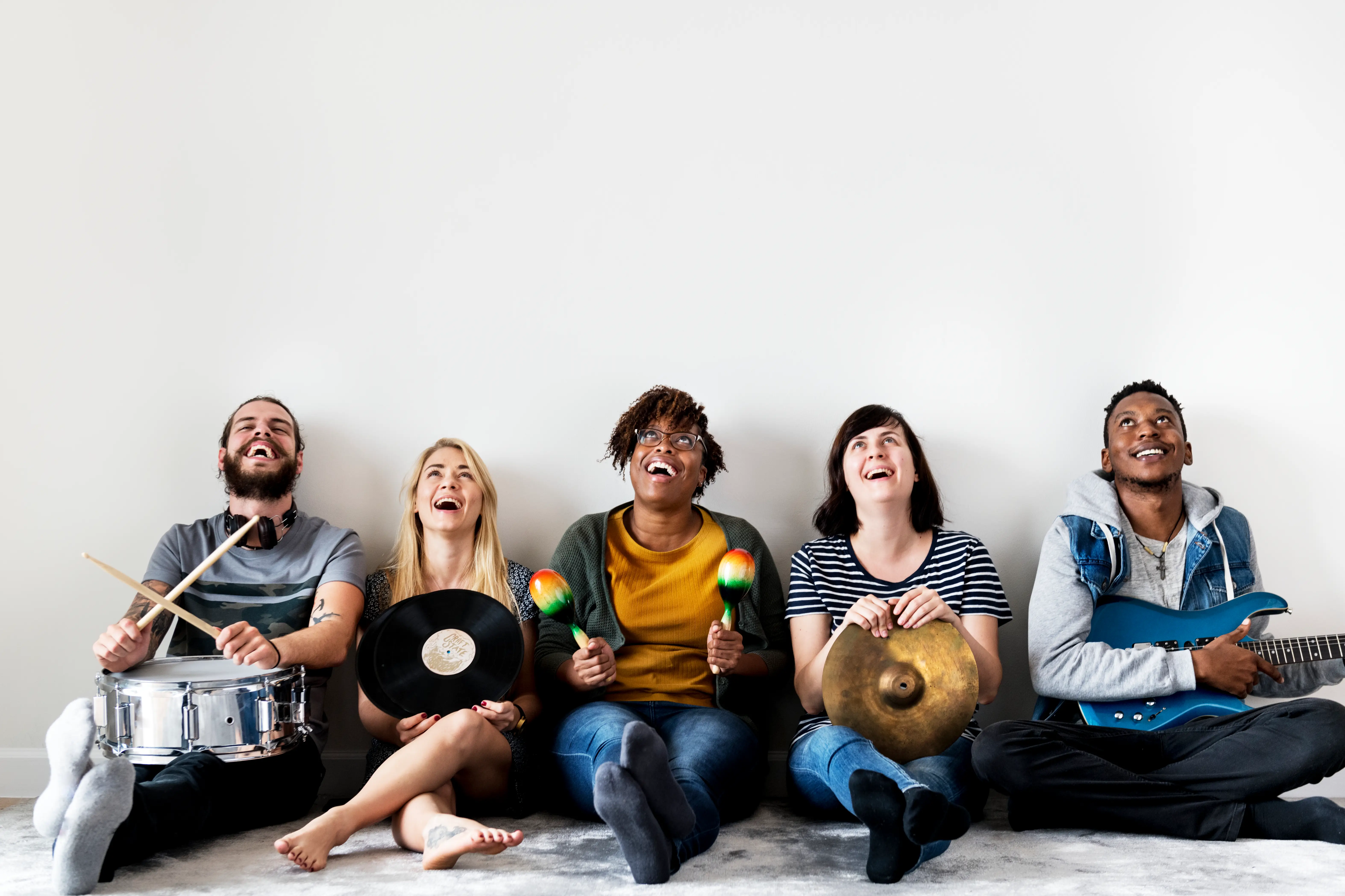 musicians sitting up against a white wall holding instruments and records
